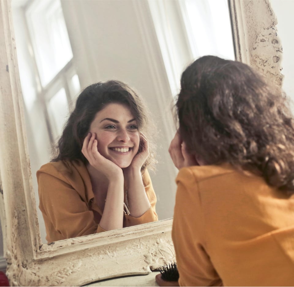 a woman smiling in front of a mirror because her thermography scan was good at well rooted women